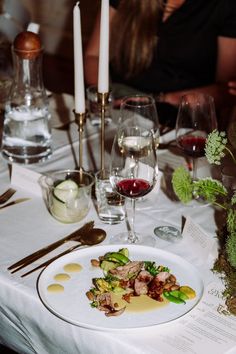 a white plate topped with meat and veggies next to a glass of wine