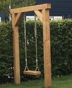 a wooden swing set in the middle of a yard next to a hedge and blue house