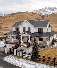 a large white house in the middle of a snow covered field with horses standing outside