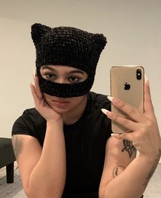 a woman wearing a black cat mask and holding up her cell phone to take a selfie