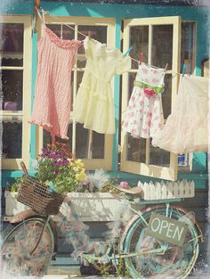 an old bicycle is parked in front of a store with clothes hanging from it's windows