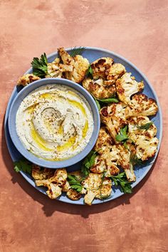 a blue plate topped with cauliflower and hummus next to a bowl of dip