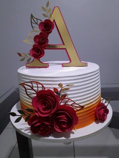 there is a white cake with red flowers on the top and gold letters at the bottom