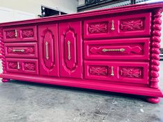 a pink dresser with ornate carvings and knobs on the doors is painted bright pink