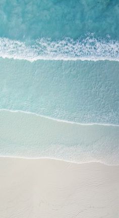 an aerial view of the ocean and beach with two people walking in the sand near the water