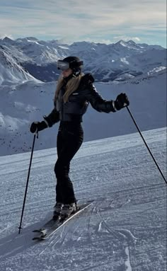 a woman riding skis down the side of a snow covered slope with mountains in the background