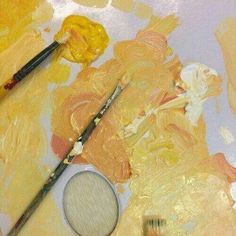 two paintbrushes sitting on top of a table next to some yellow and orange paints