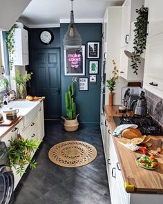 a kitchen with white cabinets and wooden counter tops next to a black door that has plants on it