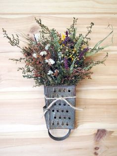 a metal grater with flowers tied to it on a wooden wall next to wood planks