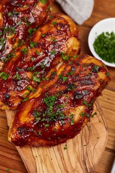 two pieces of meat sitting on top of a wooden cutting board