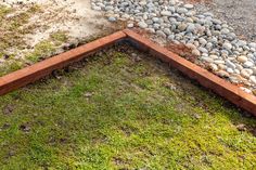 the grass is growing next to the brick planter and graveled area in front of it