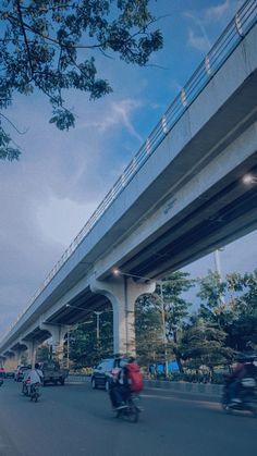 several people riding motorcycles down the street under a large overpass with traffic on it