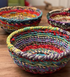 three woven baskets sitting on top of a wooden table next to each other with different colors