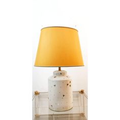 a table lamp with a yellow shade on it and a white vase sitting next to it