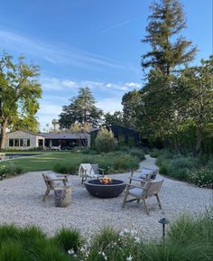 an outdoor fire pit in the middle of a gravel area surrounded by trees and bushes