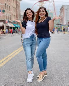 two young women posing for the camera in front of an amusement park