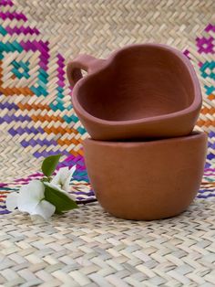 two clay bowls sitting next to each other on a woven tablecloth with white flowers