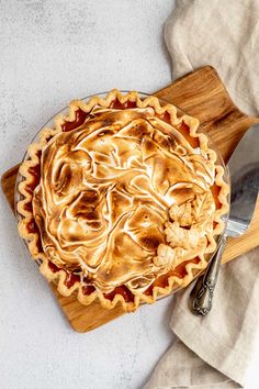 a pie sitting on top of a wooden cutting board next to a knife and fork