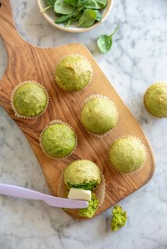 several green cupcakes on a cutting board with a bowl of greens in the background