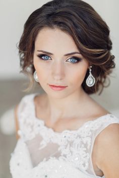 a woman with blue eyes wearing earrings and a white dress is looking at the camera