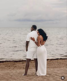 a man and woman standing on top of a sandy beach next to the ocean,