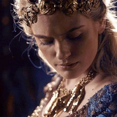 a woman in a blue dress is wearing a gold crown and looking down at her cell phone