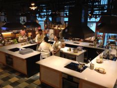 two people in a kitchen preparing food on top of a stove and counter tops with pots and pans hanging from the ceiling