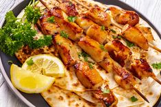 chicken skewers on a plate with lemon wedges and parsley garnish