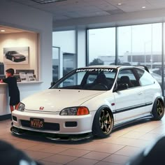 a white car parked in front of a window next to a man standing by it