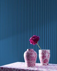 two pink vases sitting on top of a table next to a purple wall with vertical blinds