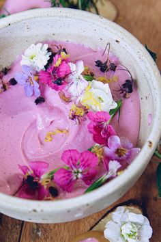 a bowl filled with pink and white flowers on top of a wooden table next to cookies