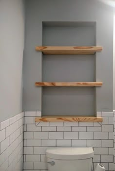 a white toilet sitting in a bathroom next to a wooden shelf above it's tank