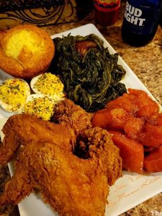 a white plate topped with fried chicken and veggies next to muffins