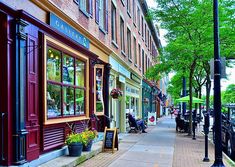 the sidewalk is lined with shops and parked cars