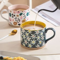 two coffee mugs sitting on top of a table next to each other with spoons