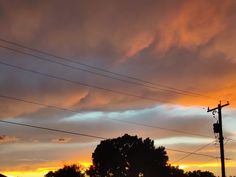 the sun is setting behind some power lines and telephone poles with trees in the foreground