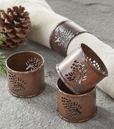 three metal canisters sitting on top of a stone floor next to a pine cone