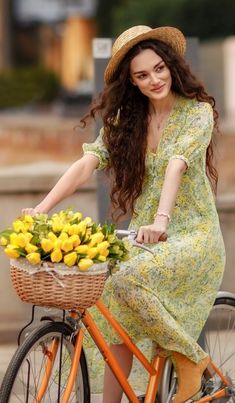 a woman riding on the back of a bike with a basket full of yellow flowers