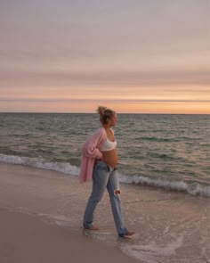 a pregnant woman walking along the beach at sunset