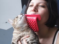 a woman holding a cat with a red brush in it's mouth as she licks the cat