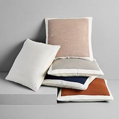 four pillows stacked on top of each other in different colors and sizes, with one folded over the edge