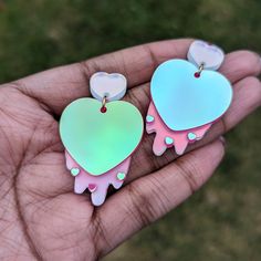 two heart shaped earrings in the palm of someone's hand with green and pink colors