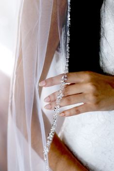 a woman wearing a wedding dress and veil with her hands on the edge of the veil