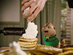 a stuffed animal is standing in front of a stack of pancakes with whipped cream on top