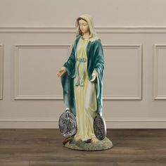 a statue of the virgin mary holding two silver coins in front of a white wall