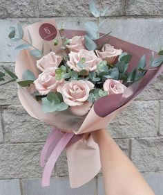 a person holding a bouquet of pink roses in front of a brick wall with greenery