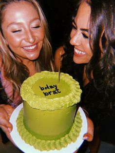 two beautiful young women standing next to each other in front of a green cake with the words baby brat on it