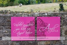 two pink signs on the side of a stone wall in front of a field with sheep