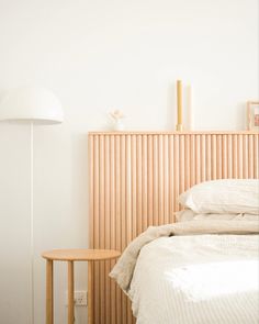 a bed with white sheets and pillows next to a wooden headboard on a wall