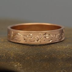 a gold wedding band that has been engraved with vines and leaves on the side, sitting on top of a rock